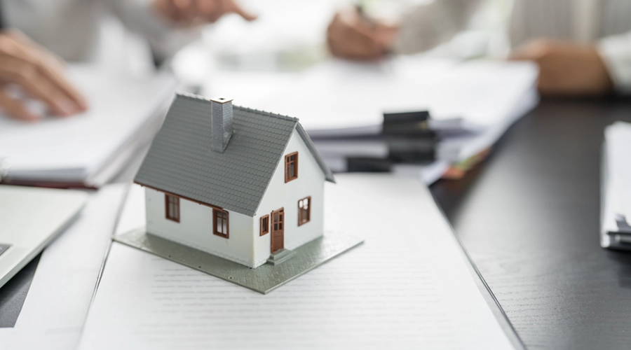 Kleines Haus auf einem Papierstapel während Verkaufsgespräch